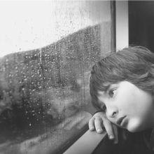 Kind sitzt traurig am Fenster